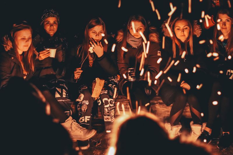 Menschen sitzen um ein Lagerfeuer. Es ist dunkel. Funken fliegen und die Gesichter sind durch den Schein des Feuers erhellt. junge Menschen sitzen im Dunklen um ein Lagerfeuer.