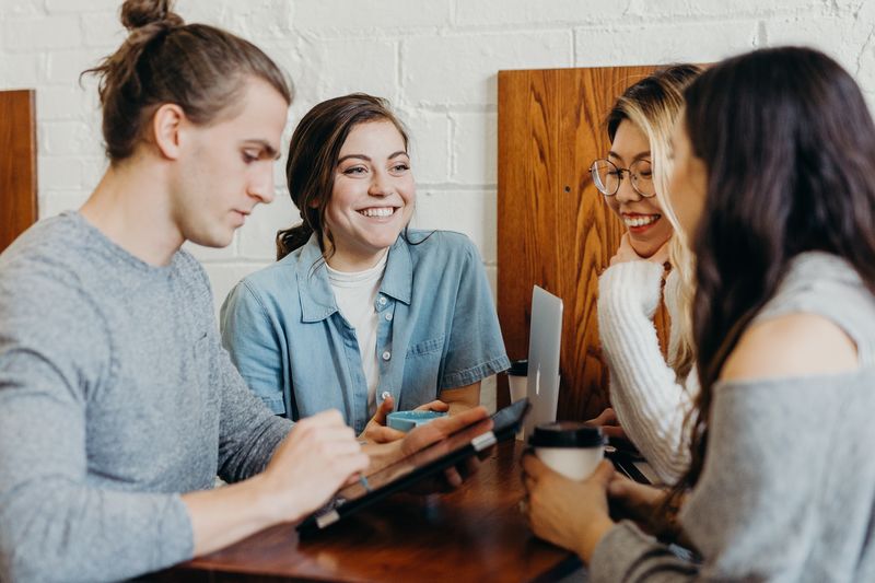 Gruppe junger Menschen trinkt gemeinsam Kaffee an einem Stehtisch und unterhält sich