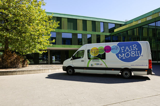 Das Fair Mobil parkt vor einer Schule, auf dem Schulhof.