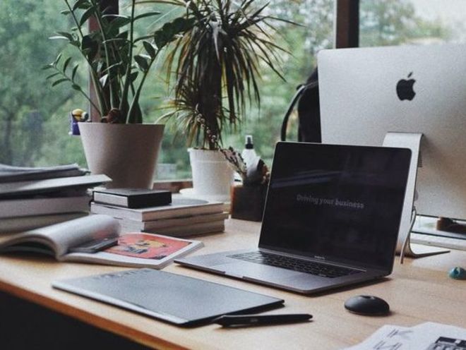 Ansicht eines Schreibtischs: Laptop, Notizen, Bücher und Büropflanzen