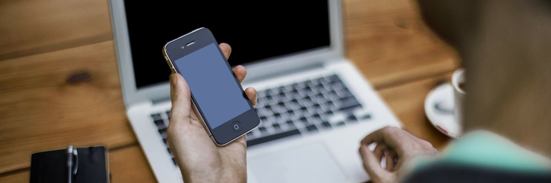 Person hält ausgeschaltetes Smartphone vor einen Laptop.